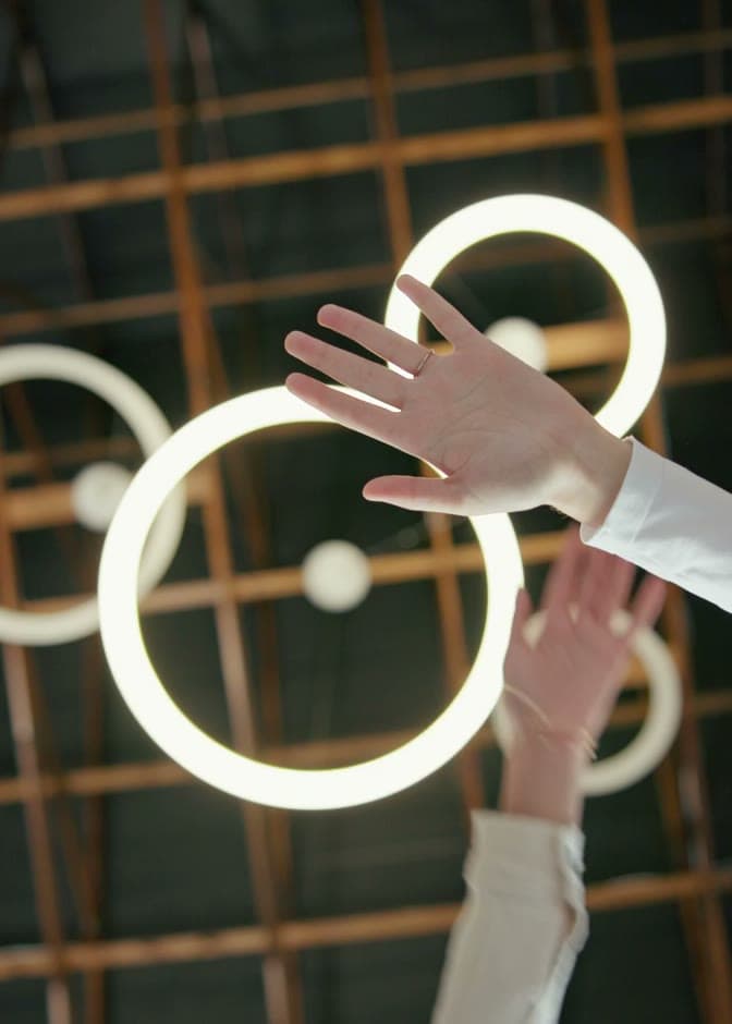 Two people reaching towards a set of illuminated rings.