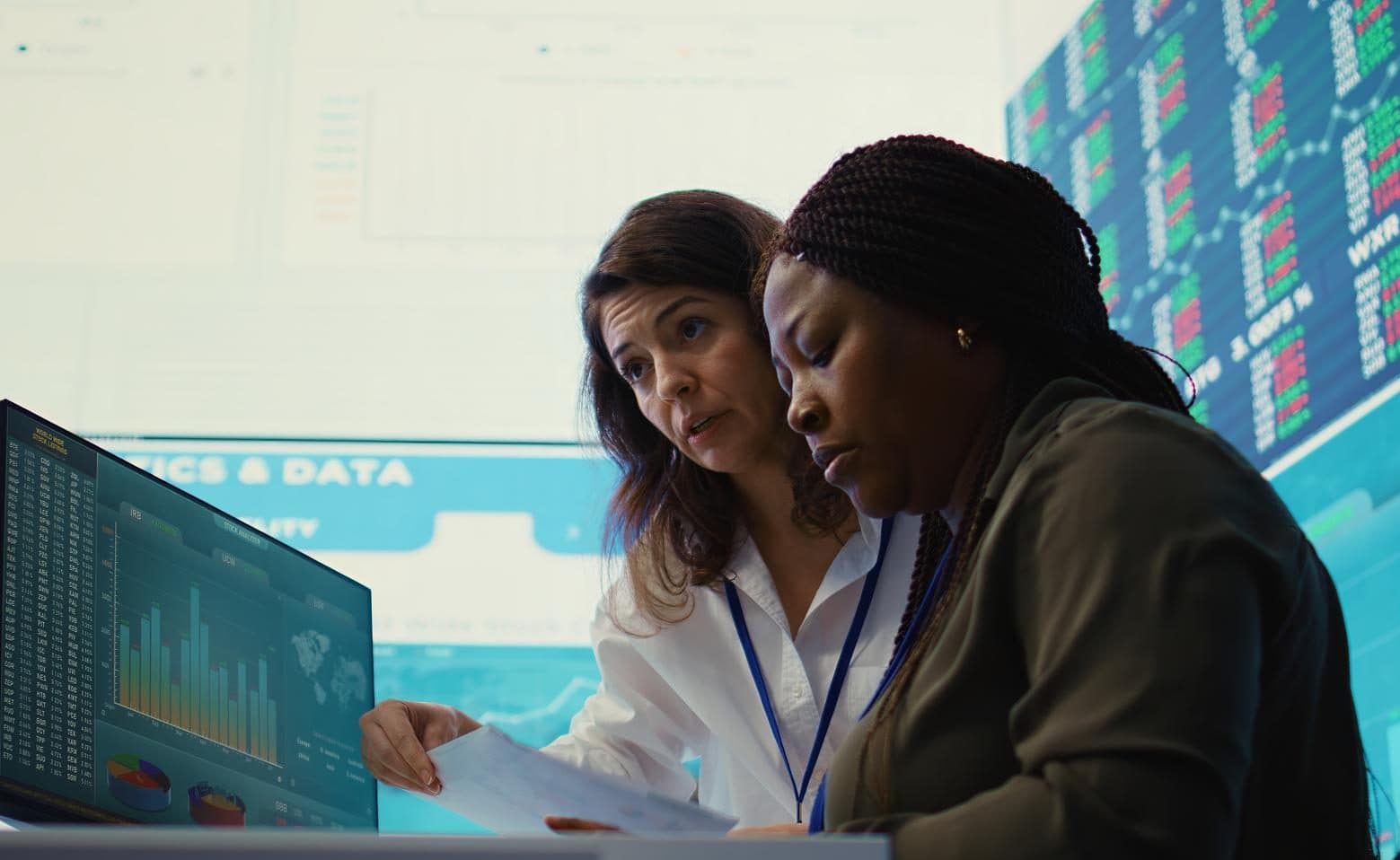 Two banking analysts reading a wall of live market and risk data.